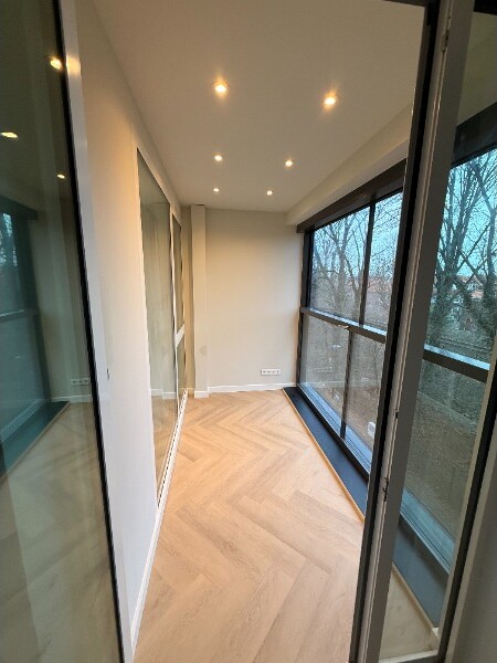 Loggia omgebouwd tot leefruimte met een houtlook PVC-vloer in visgraatpatroon en inbouwspots.