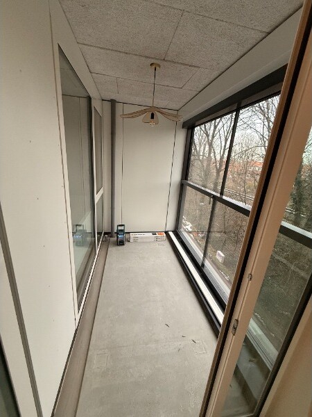 Smalle glazen loggia met een kale betonvloer en een verlaagd plafond met plafondtegels.