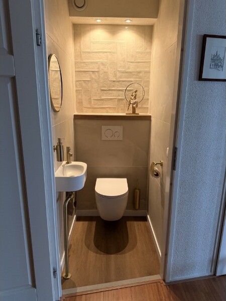 Vernieuwd toilet met een hangend closet, een visgraat-tegelwand, inbouwspots en een ronde spiegel.