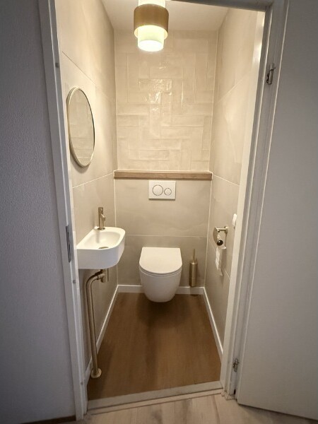 Vernieuwd toilet op de eerste verdieping, met een visgraat-tegelwand en een hangend closet.