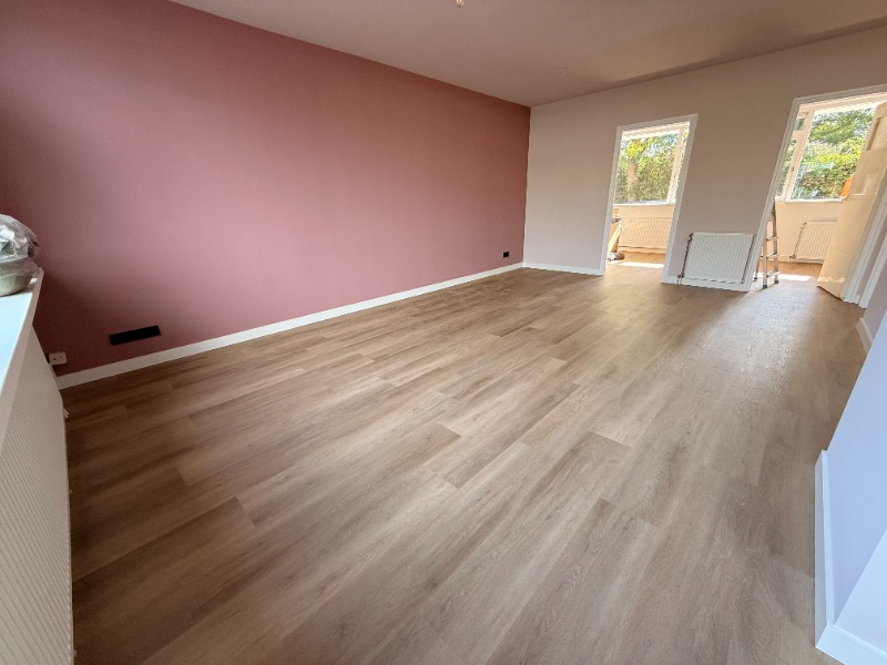 Afgewerkte woonkamer in Hillegom met een terracotta accentwand, houtlook PVC-vloer en uitzicht op de tuin.