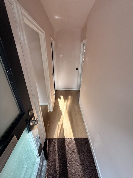 Afgewerkte gang met houtlook PVC-vloer, roze-getinte wanden en invallend zonlicht bij de voordeur.