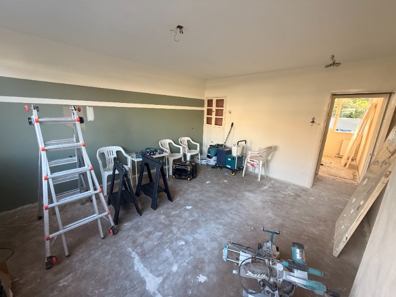 Lege woonkamer in aanbouw met kale betonvloer, een groen-wit gestreepte wand en gereedschap.