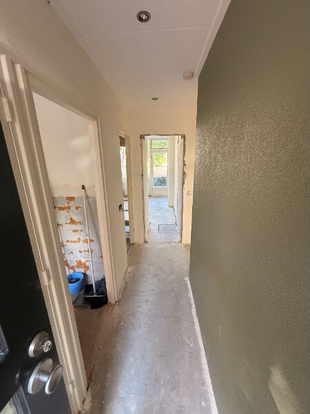 Gang in aanbouw met kale betonvloer, een groen geschilderde wand en een opengewerkte muur met kale steen.