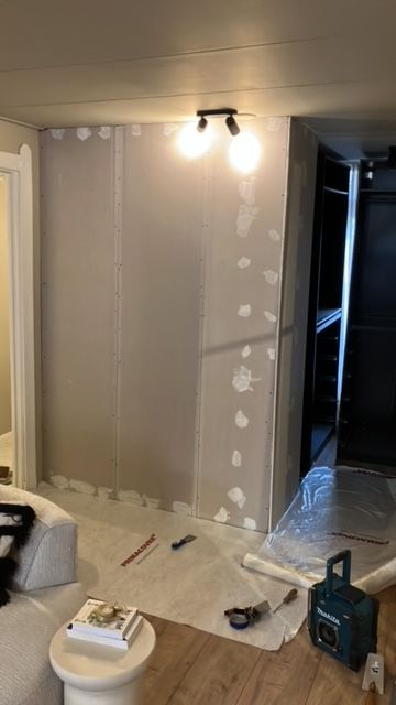 Gipsplaten wand in aanbouw met ingebouwde spots en afdekfolie op de vloer.