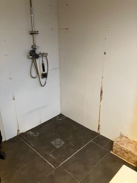 Doucheput en tegelvloer net gelegd, met een los bevestigde kraan en handdouche.