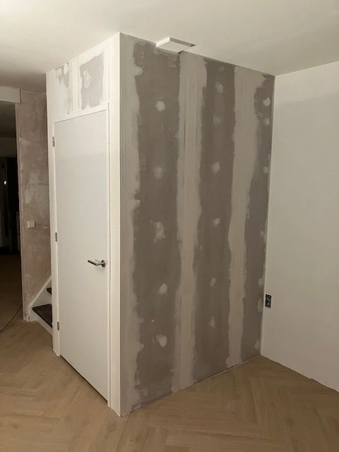 Wand onder de trap in aanbouw, ongeschilderd, met een deur.
