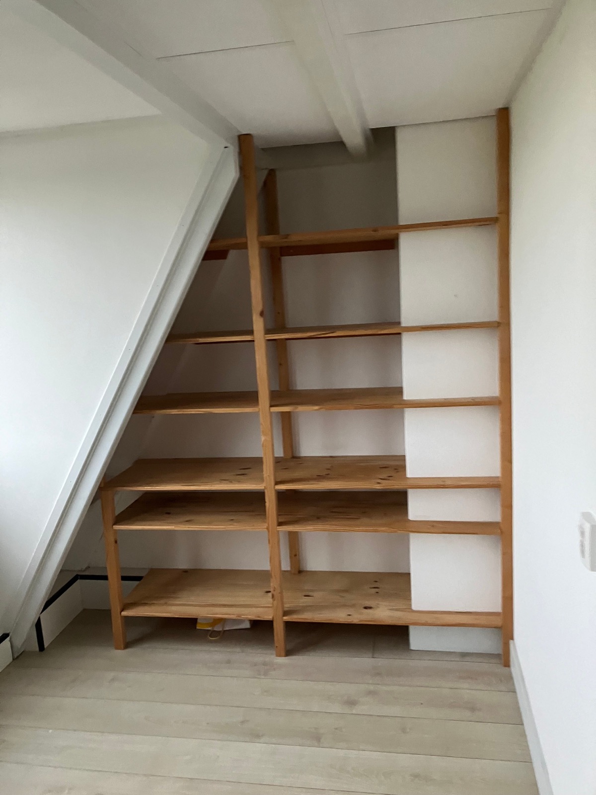 Open houten opbergschappen tegen een schuine wand.