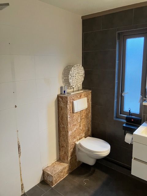 Toiletombouw in plaatmateriaal met een hangend toilet, de muur deels betegeld.