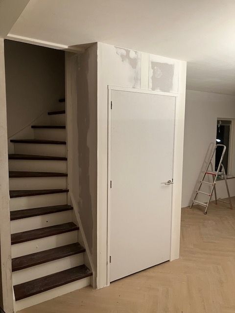 Trap met houten treden en een trapkast in aanbouw met een witte deur.