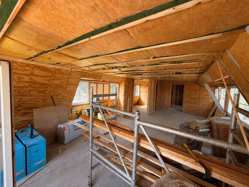 Vliering in aanbouw met een houten dakconstructie, OSB-platen tegen het dak en steigermateriaal.